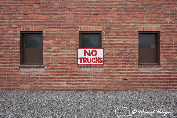 Gravel parking area and brick wall with sign, no trucks, Lovell,