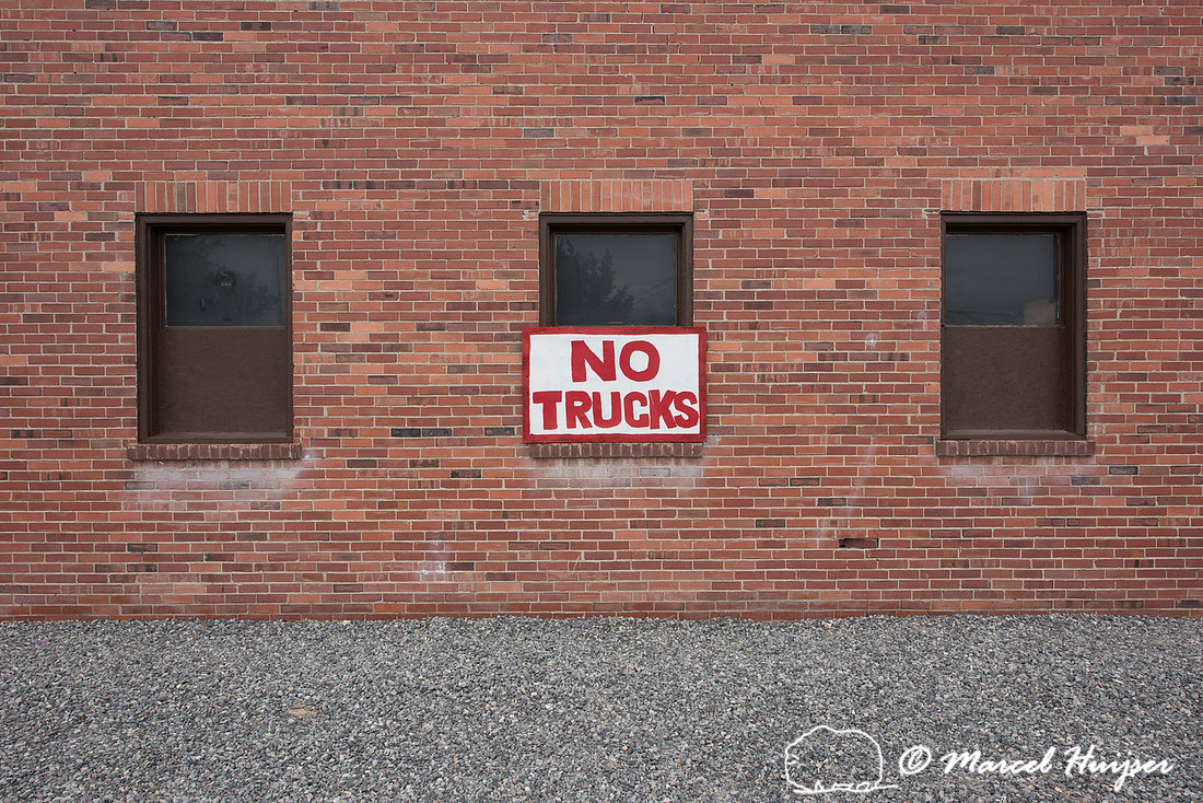 Gravel parking area and brick wall with sign, no trucks, Lovell,