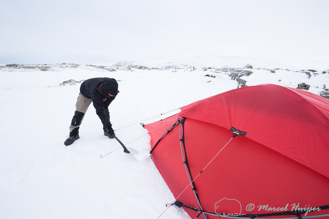 Niels Kooijman covers the lower edges of the tent with snow, Dov