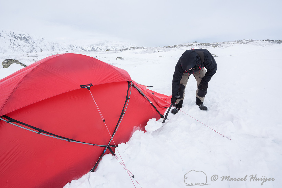 Niels Kooijman covers the lower edges of the tent with snow, Dov
