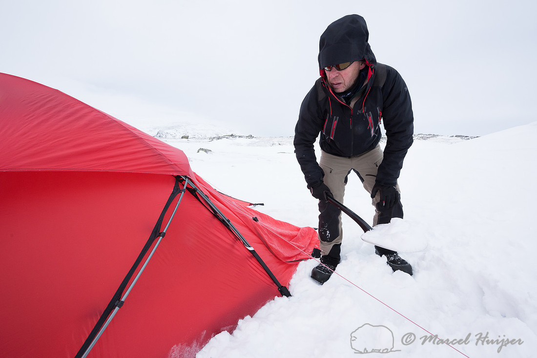 Niels Kooijman covers the lower edges of the tent with snow, Dov
