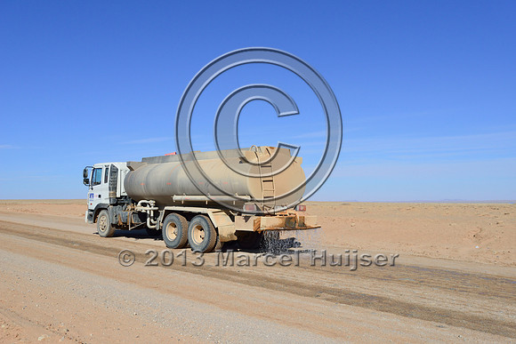 Water truck sprays water on road for dust control, Gobi, Mongolia