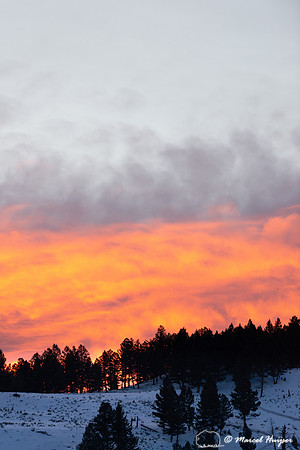 Sunset and orange clouds on snow covered hill, Wyoming