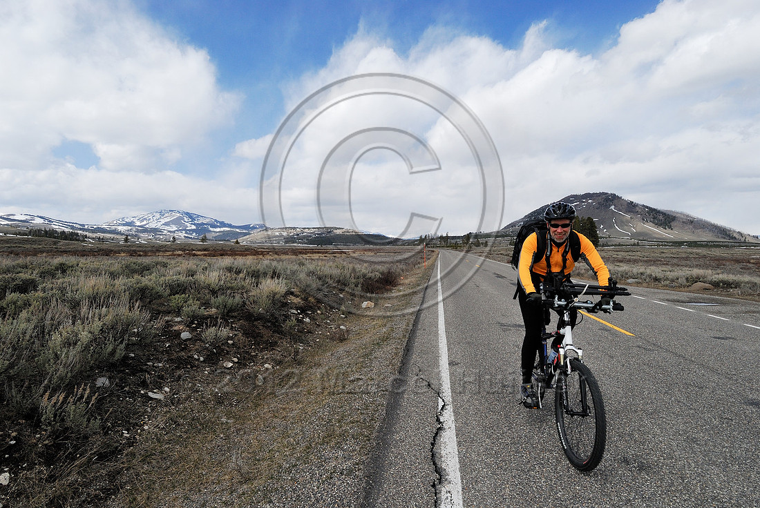 Bicyclist photographer with tripod attached to handlebars and camera backpack before roads open to motorized traffic in Yellowstone National Park, Wyoming, USA